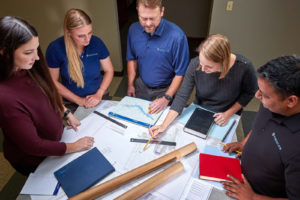 team members standing around desk looking at blueprints