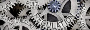 Macro photo of tooth wheel mechanism with REGULATION, LAW, RULE, AUTHORITY, GUIDELINE and STANDARD words imprinted on metal surface