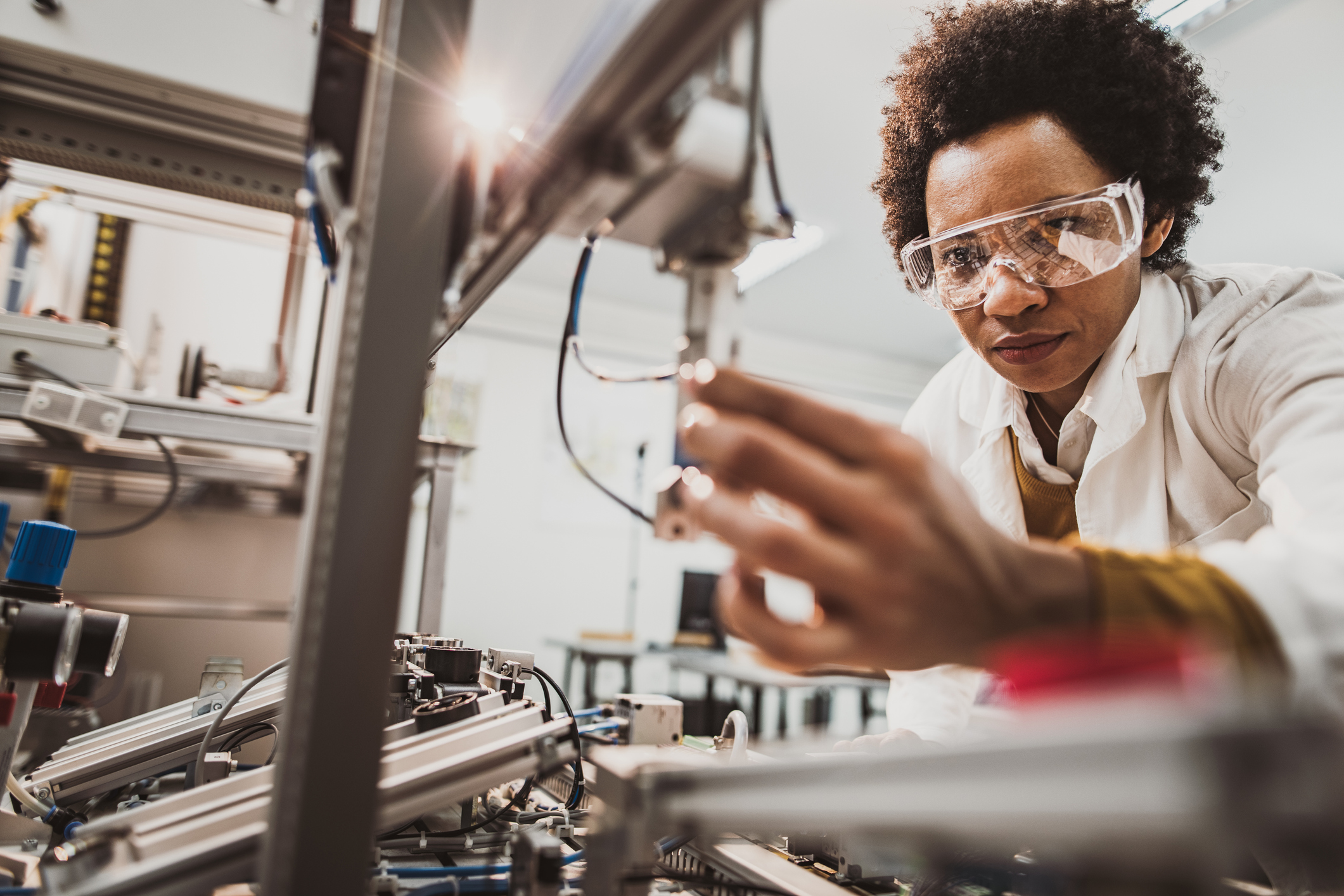 Low angle view of African American lab worker examining machine part while working in a lab.