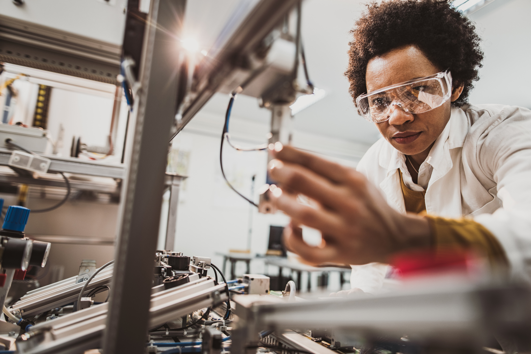 Black female engineer examining machine part while working in a lab.