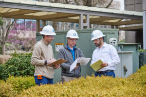 Three people in hard hats looking at notepads